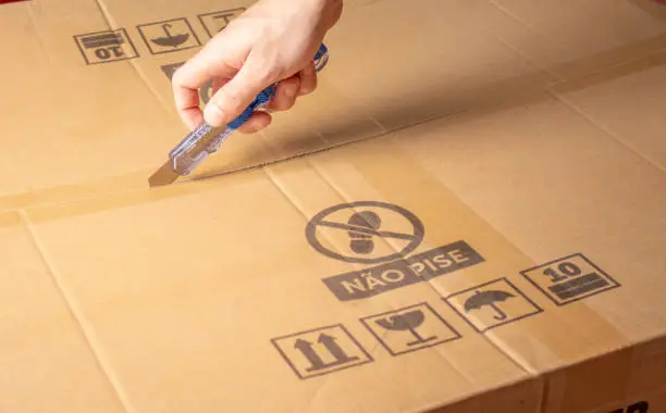 Photograph of a person's hand opening a cardboard box with the utility knife. Product and courier delivery concept.