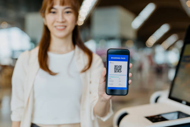 Smiling asian female traveller showing boarding pass on smartphone Image of an Asian Chinese woman showing E-boarding pass on mobile app with smartphone at self check in kiosk at airport kuala lumpur airport stock pictures, royalty-free photos & images