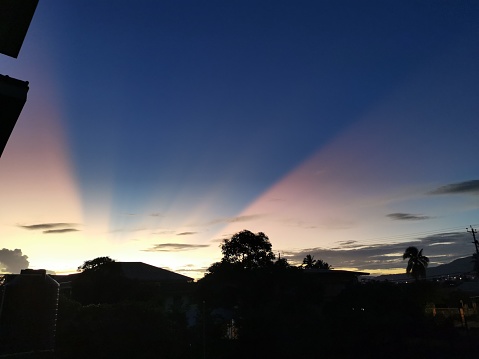 View of the pink sun rays against the blue sky. These sun rays were created by the sunset after a day of heavy rainfall in Trinidad and Tobago.