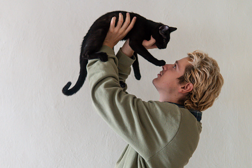 A blond boy carries his black cat while he stares at it and the cat touches it with its paw on the nose
