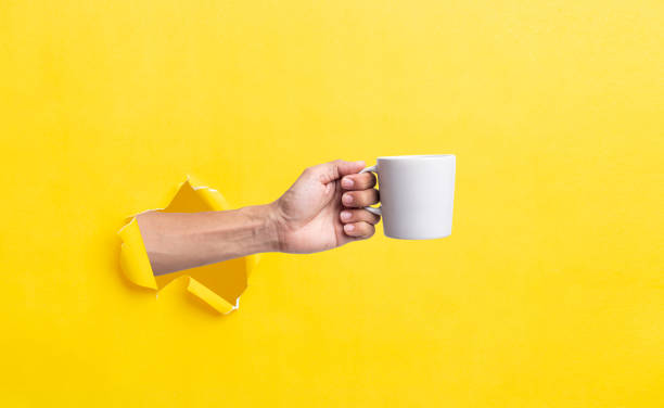 istock man hand holding a white cup on a bright yellow background 1409808452