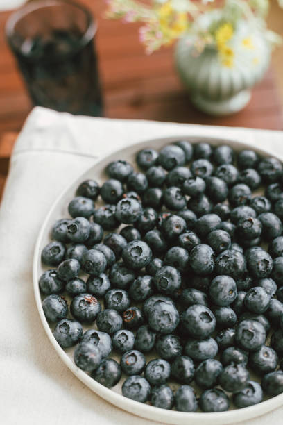 istock Fresh blueberries on modern ceramic plate and wildflowers bouquet in rustic room. Summertime in countryside. Healthy food aesthetics. Summer berries 1409810473