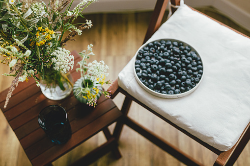 Wildflowers bouquet on background of blueberries in modern ceramic plate in rustic room. Summertime in countryside. Healthy food aesthetics. Summer berries