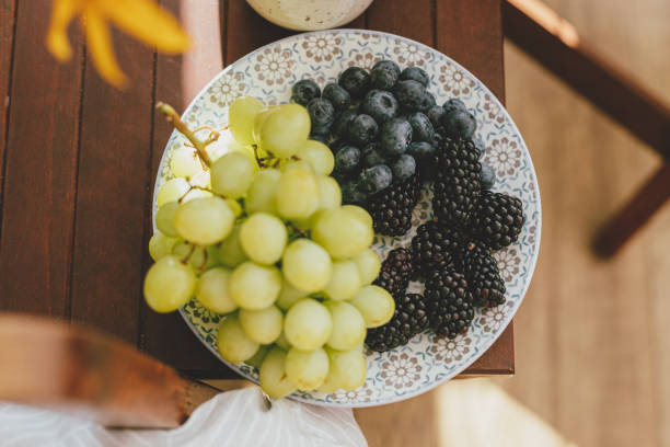 istock Fresh blueberries, blackberries and grapes in sunlight on ceramic plate in rustic room. healthy food aesthetics. Summer berries in light top view. Summertime in countryside 1409811251