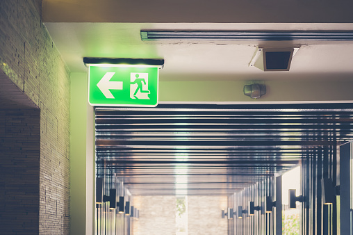 Low angle shot of illuminated green emergency exit sign suspended from the ceiling at hotel. Consists of human figure running and an arrow pointing the door.