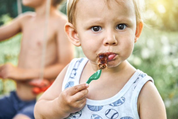 istock Cute blond toddler boy eats barbecue sausage on blurred background 1409815280