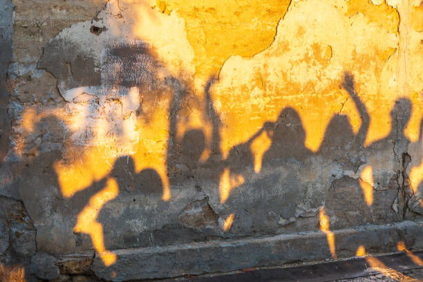 Shadows of dancing people on an old stone wall at sunset time.