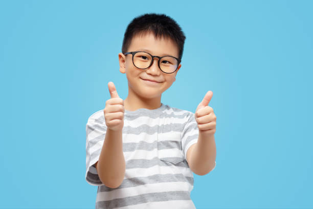 enfant heureux montrant les pouces levés, portant des lunettes sur fond bleu - glasses child little boys happiness photos et images de collection
