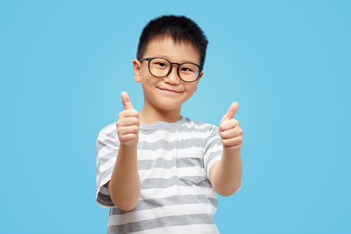 Happy kid showing thumbs up, wearing eyeglasses and tshirt on blue background