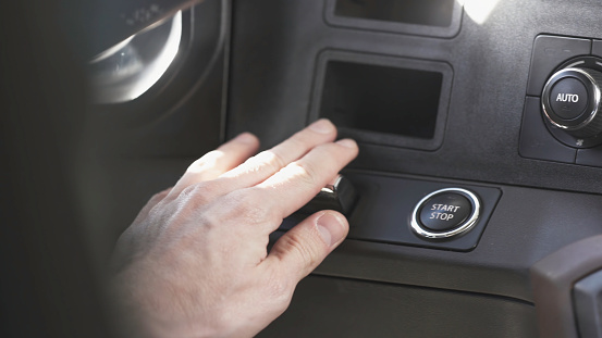 Close up of man hand pushing the car starting or stopping button to turn off the engine. View inside of a luxury expensive vehicle, driver stopping the engine by pressing the button.