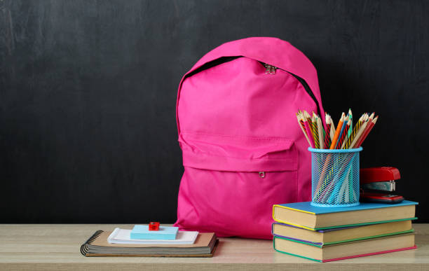 istock Pink backpack and school supplies on the table on a black background. 1409820922