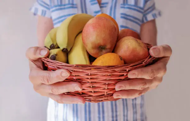 close-up, the hands of an elderly woman hold a basket with ripe fruits. healthy food concept, natural vitamins and minerals, fiber alternative to pills. Vegetarianism, proper, nutritious nutrition