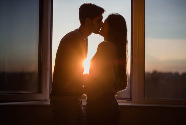 istock Affectionate couple kissing by the window at sunset. 1409822530