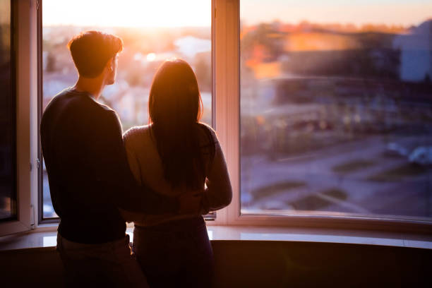 istock Back view of a couple by the window at sunset. 1409823406