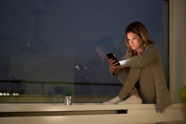 istock Young woman using cell phone by the window at night. 1409823899