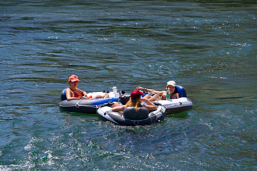Three young women in rubber boats on Limmat River on a sunny hot summer day. Photo taken June 20th, 2022, Zurich, Switzerland.