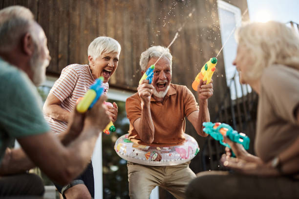 felices parejas mayores divirtiéndose durante la pelea de armas de agua en una terraza. - pistola de agua fotografías e imágenes de stock