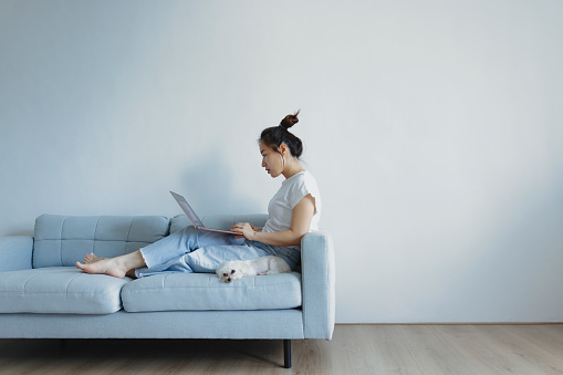 Young asian woman relaxing at home she is sitting on sofa and using laptop