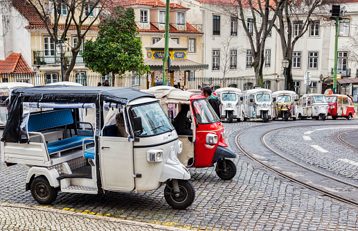 1 March 2018: Lisbon, Portugal - Covered tuk tuks ready for hire outside Lisbon Cathedral.