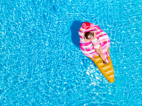A beautiful, blonde girl enjoys a hot summer day on a ice cream shaped float in the pool