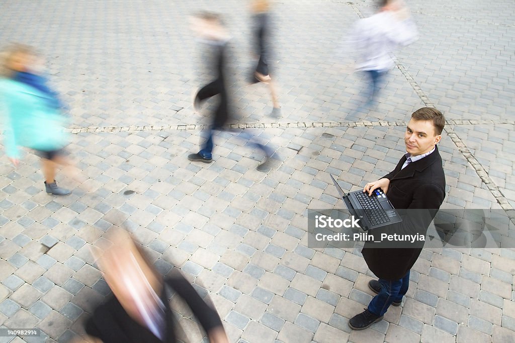 A businessman walking while carrying his laptop Young attractive businessman working on laptop through wireless technology. Motion blurred commuters walking to work Abstract Stock Photo