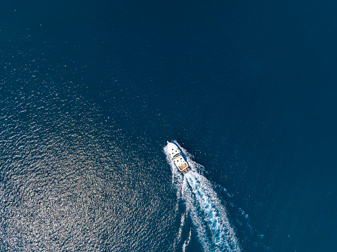Aerial top view of a motor yacht cruising over blue sea