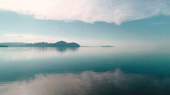 Mirrored water reflects blue sky with mountain horizon. Shot. Picturesque landscape with reflection of blue sky in quiet surface of sea. Merging sea and sky are separated by mountain horizon.