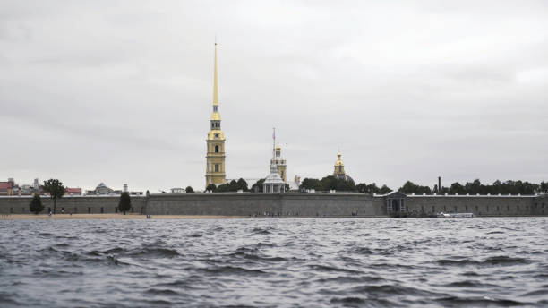 Close up of small waves of neva river and the golden spire of the Peter and Paul fortress. Action. Cloudy sky above the Petropavlovskaya fortress and Neva river. Close up of small waves of neva river and the golden spire of the Peter and Paul fortress. Cloudy sky above the Petropavlovskaya fortress and Neva river. peter and paul cathedral st petersburg stock pictures, royalty-free photos & images