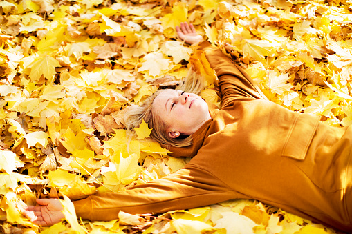 Young adult woman lying down in yellow maple leaves