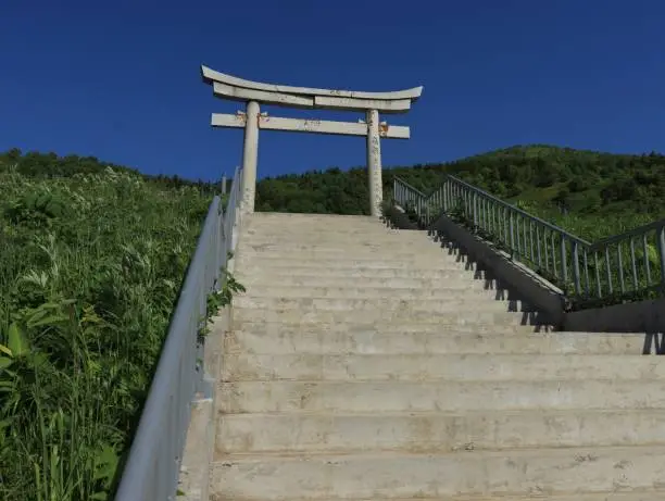 Torii gate in the village of Vzmorye on Sakhalin Island with a staircase leading to them against the blue sky; made of white marble, bottom view.