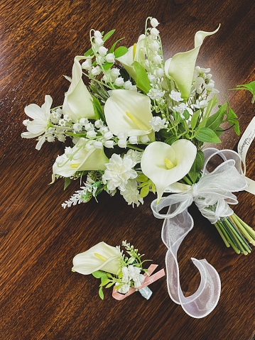 Bride holding bouquet of beautiful flowers on her wedding day, wearing an elegant white dress while sitting alone. Close up of a woman about to get married waiting with white roses and green leaves