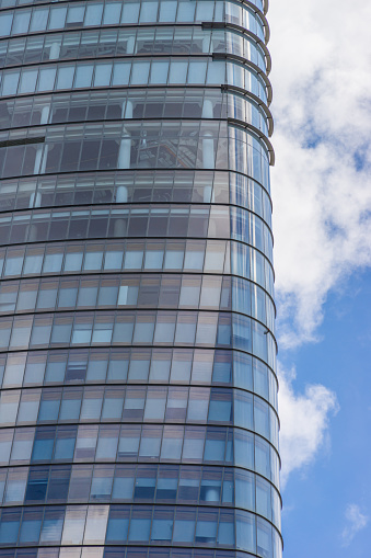 Curve glass building and dark steel window system on blue clear sky background, business concept of future architecture, modern office block with sunny beautiful sky.