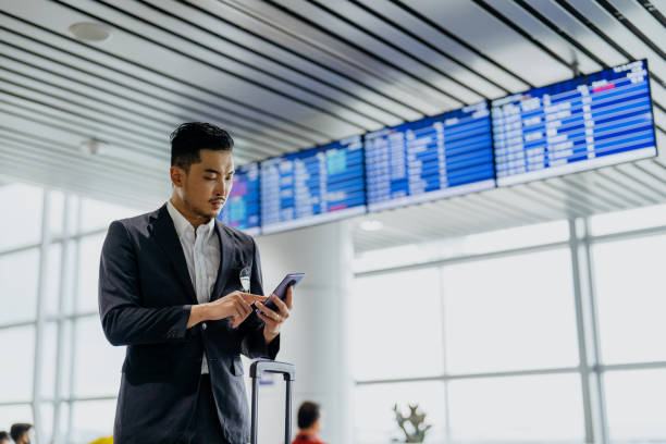 asian businessman using smartphone in airport terminal - airport business travel arrival departure board travel imagens e fotografias de stock