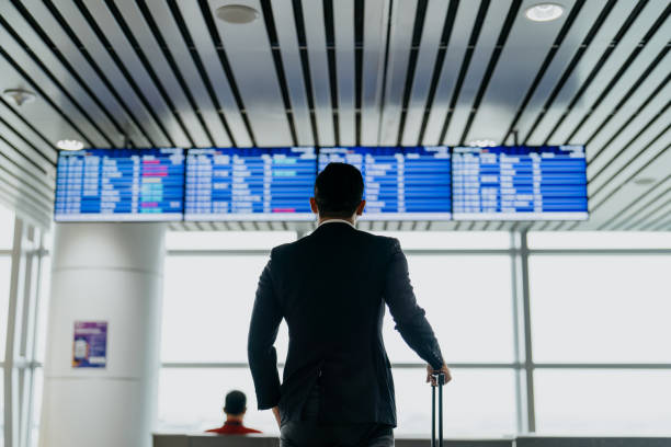 Asian businessman looking at arrival departure board in airport terminal Image of an Asian Chinese businessman traveller looking at arrival departure board in airport terminal for boarding time kuala lumpur airport stock pictures, royalty-free photos & images