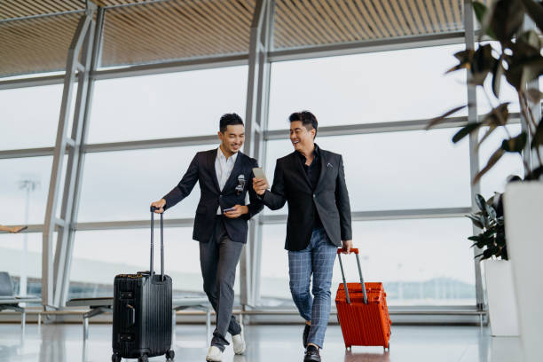 Two Asian businessmen going for a business trip by airplane Image of two Asian Chinese business travellers using smartphone and walking in airport terminal klia airport stock pictures, royalty-free photos & images