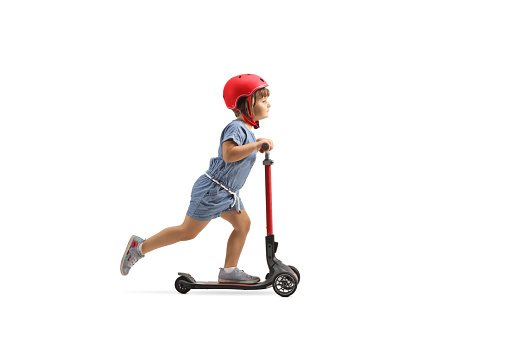 Full length profile shot of a child riding a push scooter with a helmet isolated on white background