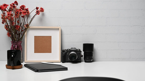 Photographer workplace with camera, digital tablet, coffee cup and picture frame on white table.