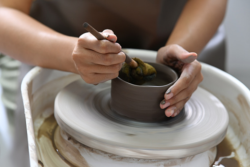 Close up view of young woman wearing apron creating handmade ceramic bowl in pottery workshop.