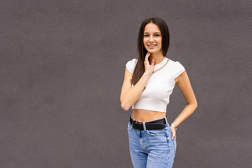 Young beautiful model wearing blank gray t-shirt and jeans posing against rough concrete wall, minimalist street fashion style