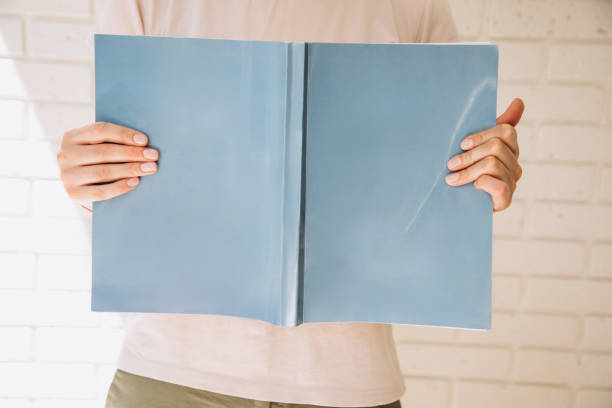 Female hands holding an open blue book with space for writing on a white brick wall background. Front view