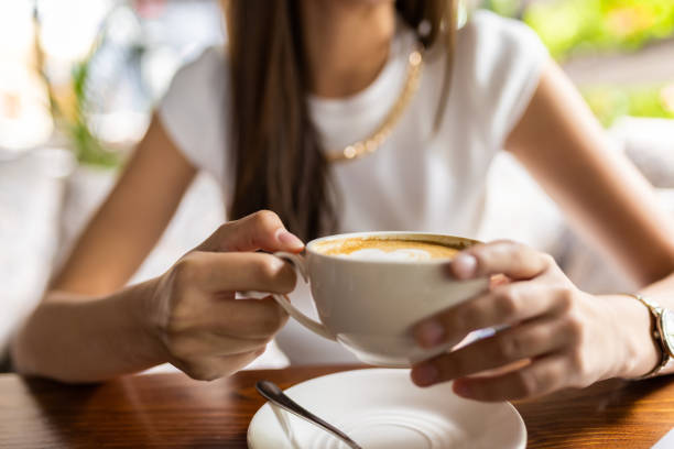 istock Close up view of female hands holding coffee cup while relaxing from work in cafe 1409843706