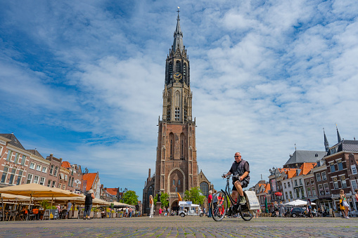Markt in Delft with the New Church tower over the Camaretten during summer with people walking and cycling over the market square.
