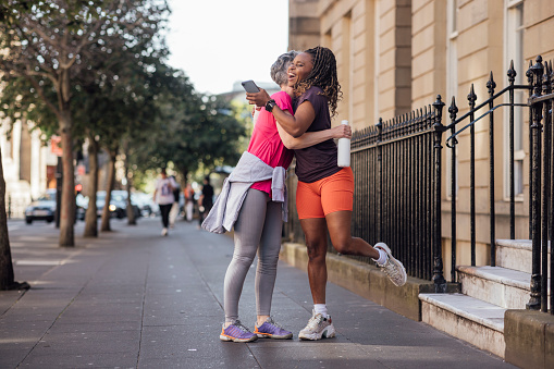 Two female friends meeting outdoors ready to go on a run together in Newcastle city centre. They are hugging while they say hello.