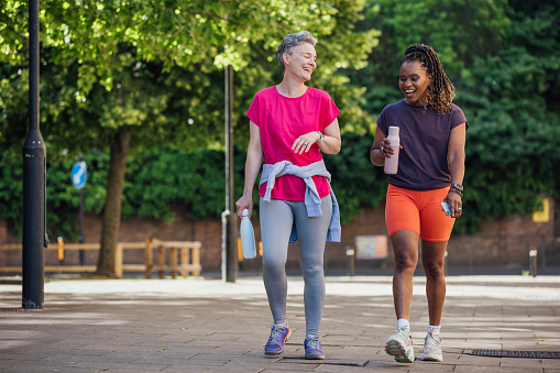 Two female friends walking together in Newcastle city centre. They are having fun, talking together carrying water bottles enjoying a summer day.