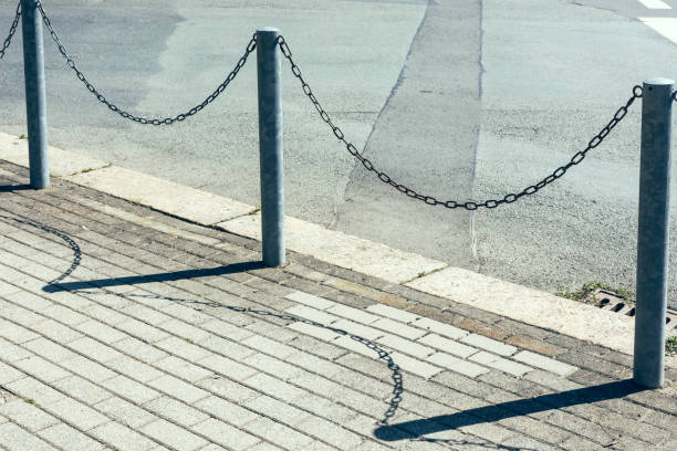 a railing with chains in front of a street in the sunshine