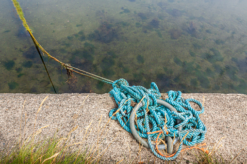 Old mooring cable tied to a metal ring on a concrete dock, boat cable, copy space. A ship's mooring cable stretched around the port ring at the harbor pier.