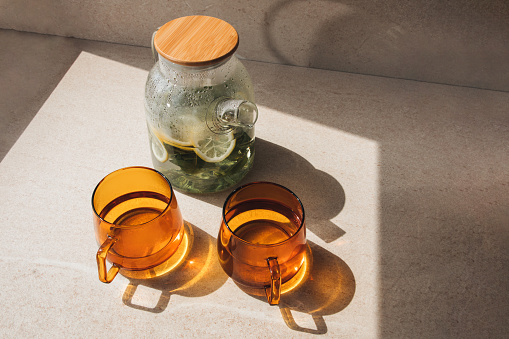 Mint tea with lemon in a glass teapot and two orange mugs on a stone background in the sunlight. Top view