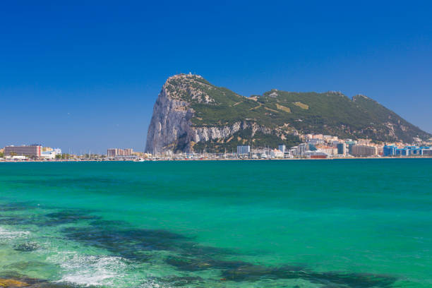 Overlooking the city and harbor of Gibraltar, ships sail on the Strait of Gibraltar, connecting the Atlantic Ocean to the Mediterranean Sea under a sunny blue sky