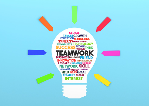 Paper in the shape of a lightbulb and the words Teamwork on it. Blue background and colorful sticky note papers.