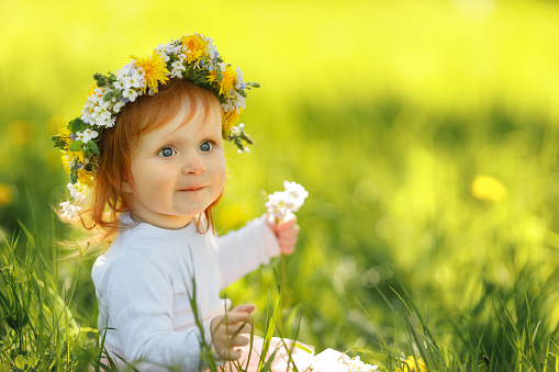 Cute little girl is wearing beautiful spring wreath outdoors, space for text. Red hair baby is spending time on nature